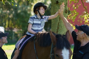 A small boy on a horse high-fives an instructor