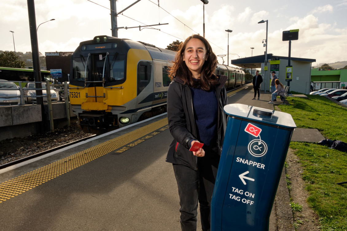 A smiling woman uses a Snapper card to tag onto a train at a station